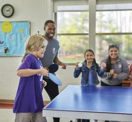 Kids and Y employees playing table tennis.