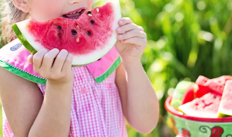 girl in pink dress eating watermelon slice
