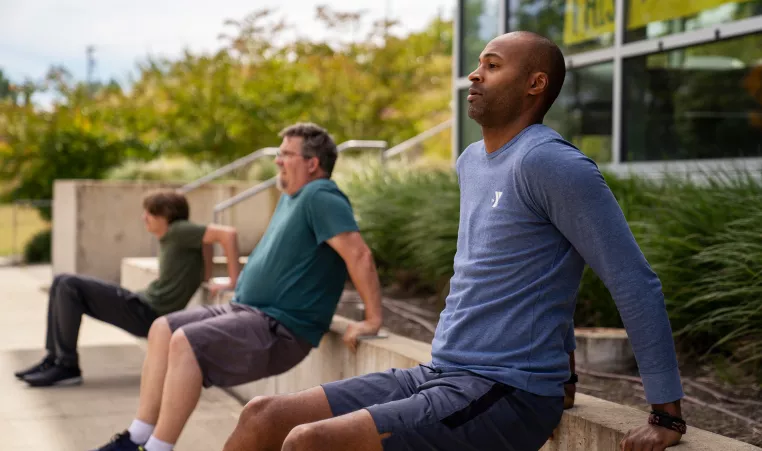 three people working out outside doing tricep dips along a cement terrace