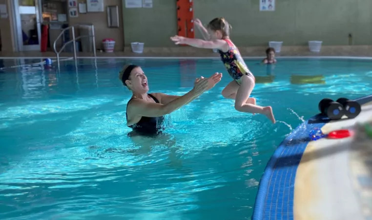 a little girl jumps into the pool with her grandma waiting to catch her