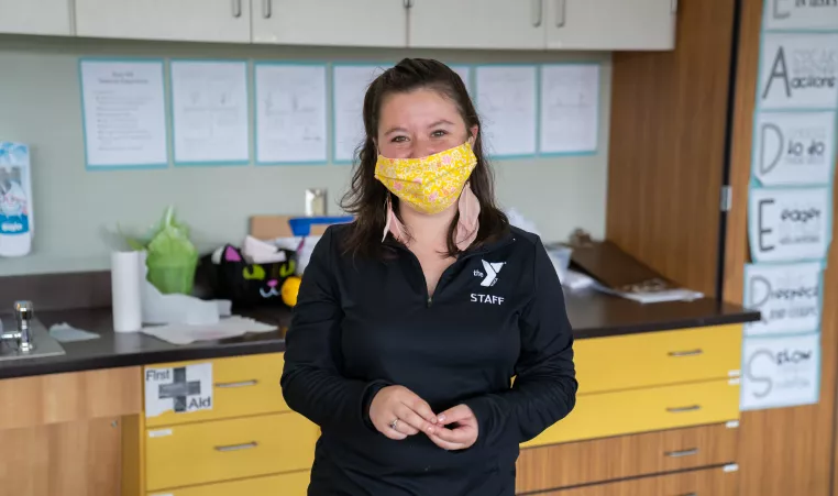 Woman in all black Y apparel smiles at the camera while wearing a face covering