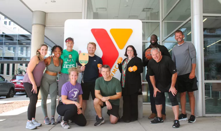 A group of YMCA members and staff in front of a Y logo sign