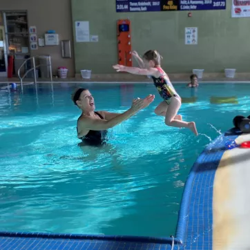 a little girl jumps into the pool with her grandma waiting to catch her