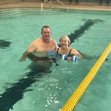 two people next to each other in the pool, one is holding water weights