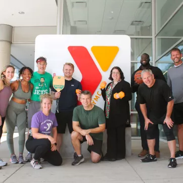 A group of YMCA members and staff in front of a Y logo sign